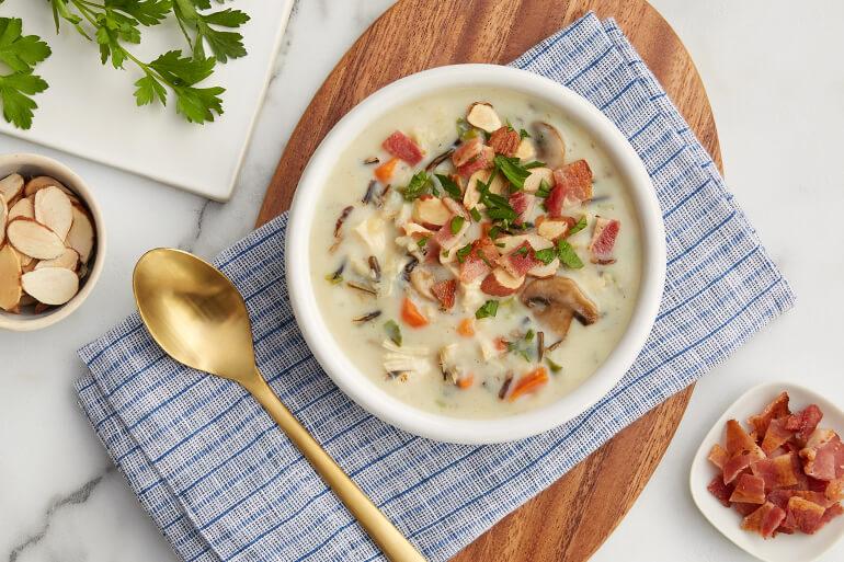 A bowl of creamy wild rice soup on a table next to a spoon