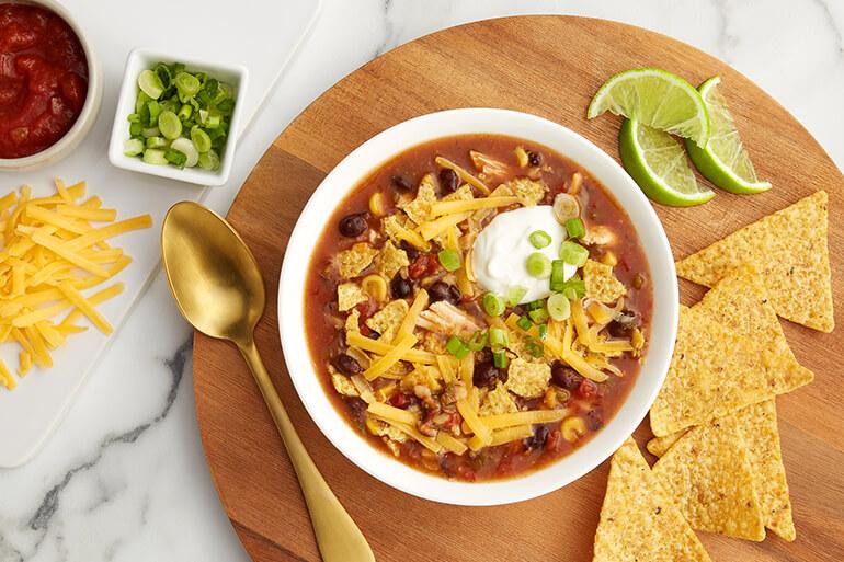 A bowl of Southwest Style Tortilla Soup on a table next to chips, limes, cheese and salsa